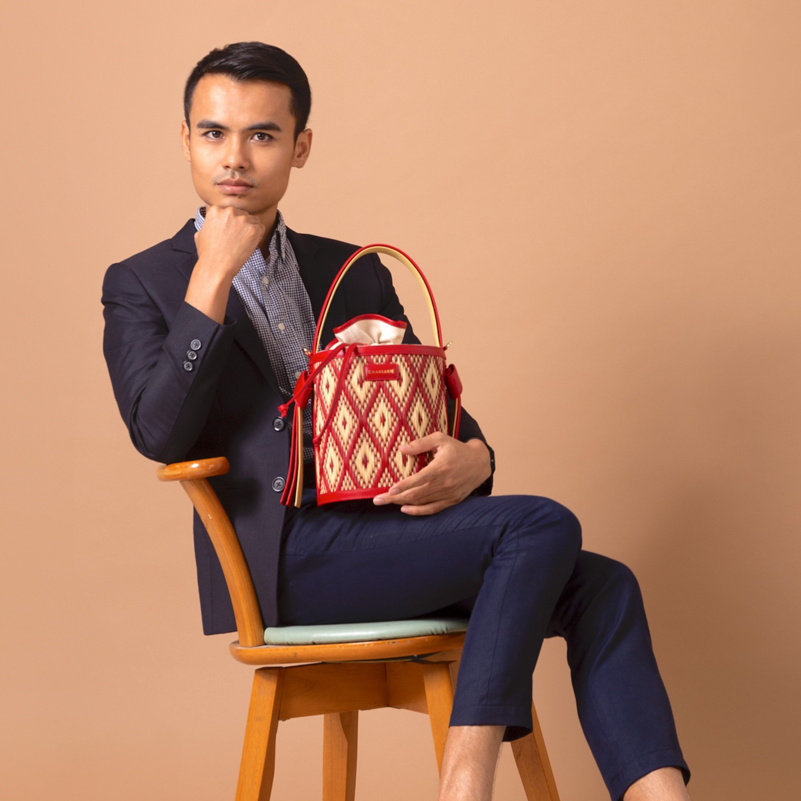 Chaksarn's Designer and CEO sitting on a chair holding a red and gold handbag against a beige background