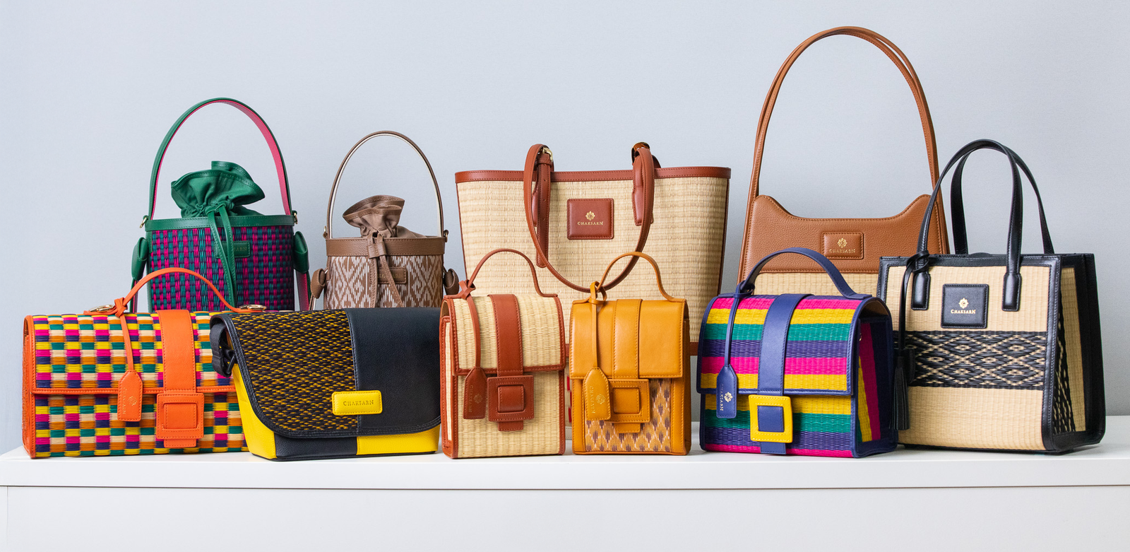 Collection of colorful woven straw handbags on a light gray background
